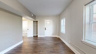 Located at 1740 N Hillside St in Wichita, Kansas, this 2-bedroom, 1-bathroom unit offers a thoughtfully laid-out single-floor plan with a clean, modern aesthetic throughout. The open living area features rich, dark hardwood-style flooring and neutral gray walls, creating a warm yet contemporary feel. Natural light filters in through window blinds, brightening the space. The kitchen runs along one wall and includes white cabinetry, white countertops, stainless steel appliances—including a dishwasher and range—and a refrigerator, with recessed lighting overhead and hardwood-style flooring continuing from the living area. The primary bedroom is a comfortable size, finished with the same dark flooring, neutral walls, and direct access to a closet. The second bedroom features a soft, patterned carpet in shades of gray and blue, a bright window, and ample wall space. Two closets provide dedicated storage throughout the unit. The bathroom is finished with large white wall tiles, a walk-in shower, a wall-mounted vanity with sink, a medicine cabinet mirror, and a natural light window. The overall design is clean, minimal, and move-in ready, offering a practical and comfortable living environment.