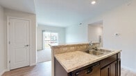 Located at 9760 Ashley River Dr. in Etna, OH, this three-bedroom, two-bathroom single-floor residence offers a well-designed layout across a comfortable footprint. The open-concept kitchen and living area serves as the heart of the home, featuring rich dark cabinetry, light granite-style countertops with a tile backsplash, black stainless appliances including a refrigerator, range, and microwave, and a large central island with breakfast bar seating. Durable wood-look flooring runs through the kitchen and living areas, while plush carpet adds warmth to the living room and all bedrooms. Sliding glass doors in the living area lead to a private balcony with neighborhood views, filling the space with natural light. The primary bedroom is generously sized and includes a spacious walk-in closet with dual wire shelving systems. Additional bedrooms each offer their own closet storage and natural light from windows. The two bathrooms are finished with tile flooring, dark vanities, and granite-style countertops. Practical amenities include a dedicated laundry area, a pantry, a utility room, and a hallway connecting the various spaces. With seven closets throughout, storage is plentiful in this thoughtfully arranged home.