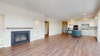 This single-floor residence offers a thoughtfully designed open-concept layout that seamlessly connects the living, dining, and kitchen areas. Light wood-tone flooring flows throughout the main living spaces, creating a warm and cohesive aesthetic. The living area features a fireplace with a sleek mantle and built-in shelving, adding both functionality and character. Large windows allow natural light to fill the space and provide outdoor views.

The kitchen is a standout feature, showcasing white shaker-style cabinetry, a grey tile backsplash, and a full suite of stainless steel appliances, including a side-by-side refrigerator, built-in microwave, and dishwasher. A dual-toned island with a crisp white countertop and steel-blue cabinetry serves as a central gathering point and adds a pop of color.

The bedrooms are carpeted for comfort and each feature ceiling fans and large windows with exterior views. The primary bathroom includes a double-sink vanity with white cabinetry, a walk-in shower, and direct access to a walk-in closet. A secondary bathroom offers a tub-shower combination with clean white tile surround. Recessed lighting throughout completes the polished, contemporary feel of this well-appointed space.