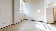 Located in downtown Winston-Salem, this two-floor suite offers a thoughtfully designed layout across a main level and an upper loft. The main level features polished concrete floors, exposed whitewashed concrete block walls, and large windows that flood the space with natural light. A ceiling fan adds comfort to the open living area. The kitchen is equipped with dark wood cabinetry, stainless steel appliances, granite countertops, a tile backsplash, and a breakfast bar. A full bathroom with a tub-shower combo and tile flooring, a half bath, and a utility closet with built-in shelving and a water heater are also found on this level. The upper loft, accessible via stairs, showcases warm hardwood floors and a whitewashed wood-plank ceiling with exposed industrial piping, creating a distinctive character.