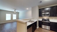 This single-story, one-bedroom, one-bathroom unit offers a thoughtfully designed layout that maximizes functionality and comfort. The kitchen serves as a central feature, showcasing dark espresso cabinetry that contrasts cleanly against light countertops. Stainless steel appliances, including a gas range, built-in microwave, and dishwasher, provide a modern, cohesive look. A peninsula with an integrated sink extends outward, creating a natural boundary between the kitchen and the living area while offering additional prep and casual dining space.

The open-concept design allows the kitchen to flow seamlessly into the living room, which benefits from a ceiling fan and a window that brings in natural light. Wood-look flooring runs throughout both spaces, adding warmth and visual continuity. Neutral wall tones and clean lines contribute to a bright, airy atmosphere throughout. Recessed lighting in the kitchen area supplements the natural light, ensuring the space remains well-lit. The overall design balances practicality with contemporary style, making efficient use of the available square footage.