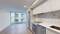 Located in the heart of downtown Montréal on Boulevard René-Lévesque Ouest, this compact yet efficiently designed 2-bedroom, 1-bathroom unit offers a contemporary urban living experience. The open-concept layout seamlessly connects the kitchen and living area, maximizing the use of every square foot on a single floor. The kitchen is a standout feature, outfitted with flat-panel white cabinetry extending to the ceiling, a striking marble-effect backsplash, stainless steel appliances including a built-in oven, dishwasher, and full-size refrigerator, and a clean white countertop. Light wood laminate flooring runs consistently throughout the unit, lending warmth and visual continuity. Large floor-to-ceiling windows in both the living area and bedrooms flood the space with natural light and offer views of the surrounding urban streetscape. The two bedrooms are clean and minimal, with crisp white walls and ample room for furnishing. The bathroom is finished with grey stone-effect tile, a glass-enclosed shower with a bench, a floating white vanity, and a large mirror. A dedicated closet and recessed lighting throughout complete this well-appointed, modern urban residence.