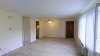 This single-floor space is organized around an open, functional layout that maximizes usability throughout. The living area is generously sized, featuring wall-to-wall carpeting that adds warmth underfoot and a ceiling fan that provides both light and air circulation. Neutral-toned walls throughout the space create a clean, versatile backdrop suitable for a variety of interior arrangements.

A passthrough or open connection links the living area to the kitchen, which is equipped with cabinetry, countertops, and standard appliances including a range. The kitchen layout is compact yet efficient, offering adequate storage and workspace.

Multiple closets are distributed throughout the unit, providing practical storage solutions. The front entry door is solid wood-toned, offering a traditional aesthetic contrast to the lighter interior palette. Windows positioned along the exterior walls allow natural light to filter into the space, contributing to a bright and open atmosphere.

The textured ceiling treatment is consistent throughout, and the overall construction reflects a straightforward residential design. The floor plan flows cohesively between areas, making the space easy to navigate and well-suited for everyday living.