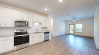 This single-floor residence offers a thoughtfully designed open-concept layout that seamlessly connects the kitchen and living areas. The kitchen is well-appointed with white shaker-style cabinetry extending to the ceiling, providing ample storage, alongside granite countertops, a white subway tile backsplash, and a full suite of stainless steel appliances including a side-by-side refrigerator with ice and water dispenser, electric range, over-the-range microwave, and dishwasher. Light wood-look flooring runs throughout the main living areas, complementing the bright, neutral color palette.

The open living area is generously proportioned, featuring a ceiling fan and a set of glass doors that allow natural light to filter in while offering access to a private outdoor space. The bedrooms are carpeted for comfort, with one featuring access to a walk-in closet equipped with wire shelving systems for organized storage. The bathroom includes a tub-shower combination with tiled surround, a granite-topped vanity, and wood-look flooring. A dedicated laundry room houses a full-size Whirlpool washer and dryer with overhead wire shelving, adding functional convenience to this well-finished space.