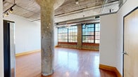 Located at 2034 Lucas Ave in St. Louis, Missouri, Unit 207 is a loft-style residence that masterfully blends industrial heritage with modern comfort. The single-floor layout offers a generous open-plan living area defined by striking architectural character, including exposed ductwork, a concrete ceiling, and original structural columns that speak to the building's industrial past. Expansive factory-style windows with brick sill detail line the main living area, inviting an abundance of natural light and offering views of the surrounding cityscape. Warm hardwood flooring runs throughout, complementing the open, airy atmosphere.

The kitchen is thoughtfully appointed with light maple cabinetry extending to the ceiling for ample storage, laminate countertops, and a suite of black appliances including a refrigerator, electric range with overhead microwave, and dishwasher. The space transitions seamlessly from kitchen to living area, making it well-suited for everyday living and entertaining.

A dedicated bathroom features dark hardwood-style flooring, white cabinetry, and clean, contemporary finishes. A modern wood-paneled door with sleek hardware adds a refined touch to the entryway. The unit also includes a closet for additional storage. Overall, Unit 207 delivers a distinctive urban living experience rooted in industrial design and filled with natural light.