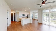 This well-appointed 2-bedroom, 2-bathroom residence in Opelika, Alabama offers a thoughtfully designed single-floor layout with a clean, modern aesthetic. The open-concept living, dining, and kitchen area serves as the heart of the home, anchored by warm hardwood-style flooring and bathed in natural light from large windows. The kitchen is a standout feature, boasting a spacious center island with a double-basin sink and quartz countertops, white upper cabinetry paired with natural wood-toned lower cabinets, a geometric tile backsplash, and a full suite of stainless steel appliances. Stylish pendant lighting and recessed fixtures illuminate the space effectively. The living area is enhanced by a ceiling fan and generous window coverage that brings in abundant outdoor views. Both bedrooms are comfortable and well-lit, each featuring ceiling fans, large windows with outdoor views, and plush carpeting. The primary bedroom offers a generous footprint. The two bathrooms are finished with modern matte black fixtures, wood-toned vanities, white quartz countertops, and tiled tub-shower combinations. A dedicated laundry area and six closets provide ample storage. A clean hallway with recessed lighting connects all areas seamlessly.