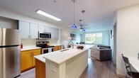Located in Seattle's vibrant Fremont neighborhood, this single-floor residence offers a thoughtfully designed open-concept layout that seamlessly connects the kitchen, dining, and living areas. The kitchen is a functional centerpiece, featuring stainless steel appliances including a refrigerator, electric range, and over-the-range microwave, complemented by warm wood cabinetry, white quartz countertops, and a spacious island with a built-in sink. Distinctive blue pendant lights add a stylish accent above the island, while a ceiling fan overhead keeps the living space comfortable. The living room is filled with natural light from large windows that frame lush greenery views, creating a bright and inviting atmosphere. Light wood-style flooring runs throughout the main areas, lending a clean, modern feel. The bedroom offers plush carpeting, a window with outdoor views, and a relaxed, restful ambiance. The bathroom is finished with a wide white vanity, ample drawer storage, wood-style flooring, and a shower-tub combination. A dedicated in-unit laundry area with a full-size washer and dryer adds everyday convenience. This residence combines practical functionality with modern finishes in a prime Seattle location.