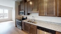 Located at 5801 Xerxes Ave N in Brooklyn Center, Minnesota, this single-floor residence offers a thoughtfully designed layout with modern finishes throughout. The kitchen serves as a central highlight, showcasing rich dark-stained cabinetry with sleek hardware, light granite countertops, and a full suite of stainless steel appliances including a range, microwave, dishwasher, and refrigerator. A kitchen island with a pendant light fixture adds additional prep space and a stylish focal point, while a double stainless steel sink and recessed lighting complete the functional design. The kitchen flows seamlessly into an open-concept living and dining area, where light-toned hardwood-style flooring extends throughout, creating a warm and cohesive aesthetic. Large windows dressed with vertical blinds allow generous natural light to fill the living space. A separate bedroom provides a quiet retreat with its own window for added brightness. The bathroom features a full-size soaking tub and shower combination with clean white surrounds and chrome fixtures. Crisp white walls, a neutral color palette, and consistent modern finishes give the entire space a clean, contemporary feel that is both functional and inviting.