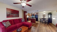 This single-floor residence offers a thoughtfully designed open-concept layout that seamlessly connects the living, dining, and kitchen areas. The living room features warm hardwood flooring, a ceiling fan with light fixture, and a sliding glass door with vertical blinds that invites natural light and provides access to the outdoors. The kitchen is a standout space, showcasing rich cherry wood cabinetry, granite countertops, a central island with additional counter space, and a full suite of black appliances including a refrigerator, electric range, built-in microwave, and dishwasher. Recessed lighting and hardwood flooring complete the kitchen's polished look. A dedicated dining area with a high-top table sits adjacent to the kitchen. The primary bedroom offers plush carpeting and a ceiling fan, providing a comfortable retreat. Additional bedrooms include a versatile room with carpet suitable as a home office or guest room, and another with bunk-bed accommodations and a bright window. Both bathrooms are finished with granite-topped cherry wood vanities, tub-shower combinations, and hardwood flooring, maintaining a consistent, cohesive aesthetic throughout the entire residence.