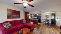 This single-floor residence offers a thoughtfully designed open-concept layout that seamlessly connects the living, dining, and kitchen areas. The living room features warm hardwood flooring, a ceiling fan with light fixture, and a sliding glass door with vertical blinds that invites natural light and provides access to the outdoors. The kitchen is a standout space, showcasing rich cherry wood cabinetry, granite countertops, a central island with additional counter space, and a full suite of black appliances including a refrigerator, electric range, built-in microwave, and dishwasher. Recessed lighting and hardwood flooring complete the kitchen's polished look. A dedicated dining area with a high-top table sits adjacent to the kitchen. The primary bedroom offers plush carpeting and a ceiling fan, providing a comfortable retreat. Additional bedrooms include a versatile room with carpet suitable as a home office or guest room, and another with bunk-bed accommodations and a bright window. Both bathrooms are finished with granite-topped cherry wood vanities, tub-shower combinations, and hardwood flooring, maintaining a consistent, cohesive aesthetic throughout the entire residence.