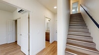 Located at 13809 E Carlisle Ave in Spokane Valley, WA, this well-designed three-story home offers 2 bedrooms and 2 bathrooms across a thoughtfully organized layout. The ground floor houses an attached garage with a modern door featuring window panels, fluorescent lighting, and side windows that bring in natural light — providing ample storage and parking space. A hallway connects the garage level to the main living areas, with light hardwood-style flooring and clean white walls setting a consistent, contemporary tone throughout. A bathroom on this level features warm wood cabinetry, a vanity with undermount sink, and a glass-enclosed shower. The main living floor is the heart of the home, combining a kitchen and living room in an open layout. The kitchen is outfitted with rich dark wood cabinetry, stainless steel appliances including a refrigerator, range, and built-in microwave, and light countertops. Both bedrooms feature light hardwood-style flooring and windows offering pleasant outdoor views of the surrounding trees, open fields, and a nearby waterway. The spacious primary bedroom benefits from multiple windows, filling the room with natural light. Two staircases connect the floors, and utility rooms provide added functionality. The scenic Spokane Valley landscape visible from the windows adds a serene, natural backdrop to this modern home.