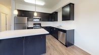 This well-designed single-floor residence offers a thoughtful layout that balances open-concept living with comfortable private spaces. The centerpiece of the home is the contemporary kitchen, which features bold dark cabinetry contrasted by light quartz countertops, a central island with pendant lighting, and a full suite of stainless steel appliances including a refrigerator, range, microwave, and dishwasher. Wood-look flooring runs throughout the kitchen and living areas, lending warmth and continuity to the space.

The open living area flows seamlessly from the kitchen, bathed in natural light from a sliding glass door that provides direct access to an outdoor space. The carpeted bedrooms offer a cozy retreat, each equipped with a ceiling fan and windows fitted with blinds for privacy and light control.

The unit includes two bathrooms. The primary bathroom features a sleek, elongated vanity with dark cabinetry and a walk-in shower, while the secondary bathroom offers a full shower-tub combination. Both bathrooms are finished with light tile flooring and clean white fixtures, maintaining a consistent, modern aesthetic throughout the home.