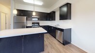 This well-designed single-floor residence offers a thoughtful layout that balances open-concept living with comfortable private spaces. The centerpiece of the home is the contemporary kitchen, which features bold dark cabinetry contrasted by light quartz countertops, a central island with pendant lighting, and a full suite of stainless steel appliances including a refrigerator, range, microwave, and dishwasher. Wood-look flooring runs throughout the kitchen and living areas, lending warmth and continuity to the space.

The open living area flows seamlessly from the kitchen, bathed in natural light from a sliding glass door that provides direct access to an outdoor space. The carpeted bedrooms offer a cozy retreat, each equipped with a ceiling fan and windows fitted with blinds for privacy and light control.

The unit includes two bathrooms. The primary bathroom features a sleek, elongated vanity with dark cabinetry and a walk-in shower, while the secondary bathroom offers a full shower-tub combination. Both bathrooms are finished with light tile flooring and clean white fixtures, maintaining a consistent, modern aesthetic throughout the home.