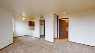Located at 5215 Mockingbird Drive in Anchorage, Alaska, Unit 308 is a single-floor residence that offers a practical and well-organized layout. The open living area is finished with wall-to-wall carpeting and neutral-toned walls, creating a clean and versatile space. Large windows allow natural light to filter in, providing views of the surrounding Anchorage neighborhood. A ceiling fan adds to the comfort of the main living space, which also features recessed lighting.

The kitchen is positioned adjacent to the living area and features warm-toned wood cabinetry, light laminate countertops with a breakfast bar overhang, a stainless steel sink, an electric range, and a refrigerator. The layout offers efficient use of space with ample upper cabinet storage.

The unit includes a generous closet with a rod for hanging storage, conveniently accessible from the main living area. The bathroom is outfitted with a full tub and shower surround in a clean, neutral finish with built-in shelving niches. An electrical panel is accessible from the entryway corridor, which also connects the key areas of the unit. The textured walls and dark wood trim throughout lend a cohesive, understated character to the interior.
