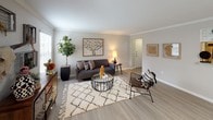 This single-floor residence offers a thoughtfully designed layout that balances comfort and style across its key living areas. The living room serves as the heart of the home, featuring light hardwood-style flooring, crown molding, and natural light streaming through blinds-fitted windows. The space is complemented by eclectic, bohemian-inspired decor, including a plush area rug, glass-top coffee table, and an accent sideboard with curated wall art, creating a warm and inviting ambiance. The adjacent dining area continues the refined aesthetic with crown molding, neutral walls, and room for a round dining table and seating, accented by framed botanical artwork. The kitchen is equipped with stainless steel appliances, including a refrigerator, electric range, and over-the-range microwave, set against white shaker cabinetry, granite-style countertops, and a classic subway tile backsplash. A dedicated laundry area is conveniently accessible directly from the kitchen. The bedroom is a serene retreat, featuring plush carpeting, a ceiling fan, and multiple windows that bathe the room in natural light. The primary bathroom impresses with a dual-vanity setup, white cabinetry, large mirrors with Hollywood-style lighting, and wood-look flooring, offering both functionality and elegance.
