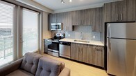 Located at 101 E Abram St in Arlington, Texas, this modern studio unit offers a thoughtfully designed open-concept layout that efficiently combines living, sleeping, and dining functions within a single, well-organized floor plan. Light wood-style flooring runs throughout, lending warmth and continuity to the space.

The living and sleeping area is designed for practical use, featuring built-in wall shelving for storage and display, along with ample room for a bed, seating, and side tables. A dedicated study or dining area with a wall-mounted desk provides a functional workspace within the unit.

The kitchen is a standout feature, outfitted with dark wood-grain cabinetry, light stone-finish countertops, a subway tile backsplash, and a full suite of stainless steel appliances including a range, microwave, dishwasher, and refrigerator. A window adjacent to the kitchen allows natural light to brighten the cooking and living area.

A spacious walk-in closet offers generous storage, while the full bathroom is clean and contemporary, featuring wood-tone cabinetry with a stone-finish countertop, a combined tub and shower with white tile surround, and wood-style flooring that matches the rest of the unit. The overall design is modern, neutral, and move-in ready.