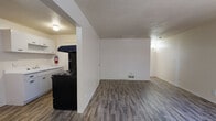 This single-floor unit offers a practical and well-organized layout designed for comfortable everyday living. The open-concept living area is generously sized, featuring dark wood-look laminate flooring, neutral white walls, and a textured ceiling that extends throughout the main living spaces. Large vertical blinds frame the front-facing windows, allowing natural light to fill the room, while a wall-mounted HVAC unit provides climate control. The living area flows naturally toward the kitchen, which is separated by a partial wall. The kitchen is equipped with a black range and overhead ventilation hood, white cabinetry, and a light-colored countertop — offering a clean, functional workspace. A full bathroom is finished with matching wood-look flooring, a combined shower and soaking tub with a window above for ventilation, and clean white fixtures throughout. The bedroom is a standout space, carpeted for comfort and featuring dual closets that provide an exceptional amount of storage. A ceiling fan with a light fixture adds both function and airflow, while a window with a blind lets in natural light. The overall ambiance of this unit is clean, move-in ready, and efficiently designed to maximize the available space on a single level.