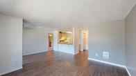 Located at 12517 E Broadway Ave in Spokane Valley, Washington, this single-story unit offers a practical and well-organized layout. The open living area is a central highlight, featuring rich wood-look hardwood-style flooring, neutral gray walls, and a textured ceiling that adds subtle visual interest. Large windows and a sliding glass door allow generous natural light to fill the space, while vertical blinds provide privacy and light control. A wall-mounted AC unit ensures comfortable climate management.

The kitchen is positioned adjacent to the living area and features a pass-through breakfast bar that promotes an open, connected feel. Light wood cabinetry provides ample storage, complemented by a continuous countertop with an integrated sink, a dishwasher, and a white electric range with overhead ventilation.

The bedrooms are carpeted for comfort and each includes a baseboard heater, a closet with sliding doors, and windows overlooking greenery outside. The primary bedroom connects to a vanity area with dark countertops, ample cabinetry, and direct access to a private toilet and shower room. A second full bathroom features light wood cabinetry, a single-basin sink, and wood-look flooring. The unit also includes a dedicated entryway providing a welcoming transition into the living space.
