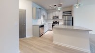 Located at 100 Harley Ln in Pooler, Georgia, this single-floor residence offers a well-designed, open-concept layout that seamlessly connects the living and kitchen areas. The kitchen is a standout feature, equipped with stainless steel appliances including a range, over-the-range microwave, dishwasher, and refrigerator. Gray shaker-style cabinetry pairs with granite countertops and a classic subway tile backsplash, while light hardwood-style flooring, a central island with pendant lighting, and a built-in wine rack add both function and style. The open living area flows naturally from the kitchen, featuring plush carpeting, a ceiling fan, and a large window that invites natural light. The bedrooms are carpeted and bright, each with large windows fitted with blinds for privacy. At least one bedroom includes access to a walk-in closet with built-in shelving. The bathroom is finished with granite countertops on gray cabinetry, light wood-look flooring, a soaking tub and shower combination with tiled surround, and a well-lit vanity mirror. Throughout the space, neutral tones and consistent finishes create a clean, cohesive aesthetic.