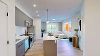 Located at 1750 4 St NE in Calgary, this thoughtfully designed two-bedroom, two-bathroom residence offers a clean, modern aesthetic throughout its efficiently laid-out single floor. The kitchen serves as a focal point, featuring sleek matte grey cabinetry extending to the ceiling, white quartz countertops, stainless steel appliances, a subway tile backsplash, and a central island with seating — all illuminated by recessed lighting and a contemporary pendant fixture. Light oak-toned flooring flows consistently throughout, reinforcing the space's bright and cohesive feel. The primary bedroom is a calm retreat, complete with a built-in closet and direct access to a private ensuite bathroom featuring a glass-enclosed shower, light wood vanity cabinetry, and large-format tile work. The second bedroom benefits from generous natural light through oversized windows with treetop views and features a distinctive patterned accent wall. A second full bathroom includes a soaker tub with tiled surround and a matching wood-toned vanity. A dedicated closet provides additional storage. Throughout the unit, matte black hardware accents, white walls, and consistent flooring create a refined, contemporary atmosphere suited to modern living.