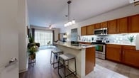 This single-story, one-bedroom, one-bathroom residence in Mansfield, TX offers an efficiently designed layout that maximizes functionality throughout. The open-concept kitchen and living area serves as the heart of the space, where the kitchen stands out with warm honey-toned cabinetry, granite countertops, a tiled mosaic backsplash, and a full suite of stainless steel appliances including a refrigerator, range, and microwave. A central island with a built-in sink and granite surface provides additional workspace and doubles as a breakfast bar with seating for multiple guests. Pendant lighting overhead adds a polished finish to the kitchen area. The adjacent living room features wood-style flooring, a ceiling fan, and floor-to-ceiling sliding glass doors with vertical blinds that open to a private patio, bringing in generous natural light and outdoor views. The bedroom features plush carpeting, a ceiling fan, and a window with natural light. The bathroom includes tile flooring, a granite-topped wood vanity, and a full tub-shower combination with tile surround.