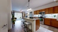 This single-story, one-bedroom, one-bathroom residence in Mansfield, TX offers an efficiently designed layout that maximizes functionality throughout. The open-concept kitchen and living area serves as the heart of the space, where the kitchen stands out with warm honey-toned cabinetry, granite countertops, a tiled mosaic backsplash, and a full suite of stainless steel appliances including a refrigerator, range, and microwave. A central island with a built-in sink and granite surface provides additional workspace and doubles as a breakfast bar with seating for multiple guests. Pendant lighting overhead adds a polished finish to the kitchen area. The adjacent living room features wood-style flooring, a ceiling fan, and floor-to-ceiling sliding glass doors with vertical blinds that open to a private patio, bringing in generous natural light and outdoor views. The bedroom features plush carpeting, a ceiling fan, and a window with natural light. The bathroom includes tile flooring, a granite-topped wood vanity, and a full tub-shower combination with tile surround.