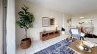 This single-floor residence offers a thoughtfully arranged layout across several distinct living spaces. The living room serves as the central gathering area, featuring light tile flooring, neutral walls, and an arched opening that leads to a private balcony with outdoor views of surrounding greenery. Adjacent to the living room, the dining area benefits from an open connection to both the living space and kitchen, with a pass-through window adding architectural interest and enhancing the sense of openness.

The kitchen is equipped with white cabinetry featuring decorative hardware, a drop ceiling with grid paneling, tile flooring, and full-size appliances including an electric range and a top-freezer refrigerator. A light countertop runs along the perimeter, providing functional workspace.

Both bedrooms are carpeted and bathed in natural light from multiple windows. The primary bedroom is generously sized and includes a walk-in closet. An additional flexible room with carpet and a louvered closet door offers versatile use as a guest room, office, or play area.

Two full bathrooms each include a tub-shower combination with tiled surrounds, a vanity with storage below, and tile flooring, maintaining a clean and cohesive aesthetic throughout the residence.