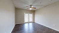 Located at 4925 Cromwell Dr in Kyle, Texas, this single-story residence offers a well-organized layout with a cohesive design throughout. The open living area is a standout feature, showcasing rich, dark hardwood-style flooring that extends across the main living spaces. A ceiling fan with integrated lighting keeps the room comfortable, while French doors with blinds invite natural light and provide outdoor access, enhancing the overall sense of openness.

The kitchen is positioned adjacent to the living area, separated by a granite-topped peninsula that serves as both a functional workspace and a visual divider. Dark espresso cabinetry pairs with granite-style countertops, and the kitchen is equipped with black appliances including a refrigerator, microwave, and range. The hardwood-style flooring continues seamlessly into this space.

The bedrooms are finished with plush wall-to-wall carpeting, providing a warm contrast to the hard flooring in the main areas. Each room includes a ceiling fan and window with blinds. The primary bedroom features direct access to a spacious walk-in closet with built-in shelving. The bathroom is appointed with white subway tile in the tub surround accented by a decorative earth-toned tile band, dark wood cabinetry with granite countertops, and matching hardwood-style flooring. The neutral color palette throughout creates a clean, move-in-ready atmosphere.