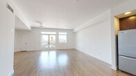 This contemporary single-floor residence offers a thoughtfully designed open layout with clean lines and a bright, airy aesthetic throughout. Light wood flooring flows seamlessly across the main living areas, complementing the crisp white walls and adding warmth to the modern interior.

The expansive living area is bathed in natural light through large windows and glass French doors, which open to views of the surrounding cityscape, including glimpses of palm trees that hint at a warm urban setting. The space feels generous and versatile, well-suited for both relaxing and entertaining.

The kitchen is outfitted with rich dark wood cabinetry, a full suite of stainless steel appliances including a refrigerator, range, microwave, and dishwasher, along with a central island that provides additional prep and storage space. Recessed lighting illuminates the kitchen efficiently.

The bedrooms continue the light wood flooring and benefit from oversized windows that frame city views while filling each room with natural light. Each bedroom provides convenient access to a well-appointed bathroom.

The bathrooms feature dark wood vanities with clean white countertops, framed mirrors with accent lighting, and a combination tub and shower with sliding glass doors. The primary bathroom includes a double-sink vanity with a wide mirror, offering a refined and functional finish throughout.