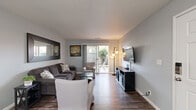 Located at 1700 N Tully Rd in Turlock, California, this single-story 2-bedroom, 1-bathroom home offers a comfortable and efficiently designed layout. The living room serves as the heart of the home, featuring rich hardwood-style flooring, neutral gray walls, and a sliding glass door that fills the space with natural light and provides direct access to a private outdoor patio. The galley-style kitchen is outfitted with white cabinetry, light countertops, a stainless steel sink, and a gas range, offering ample storage and functionality. Adjacent to the kitchen, the dining area accommodates a round table and is brightened by a window with blinds and a ceiling fan overhead. The primary bedroom is a well-proportioned retreat with hardwood-style flooring, a ceiling fan, and generous wall space. The second bedroom features a large window dressed with floor-length curtains, allowing for natural light while maintaining privacy. The full bathroom is finished with a white vanity, a combination tub and shower, and hardwood-style flooring, all set against a cool gray palette. A dedicated closet provides additional storage throughout. Consistent flooring, neutral tones, and clean lines give the entire home a cohesive, modern feel.