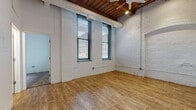 Located on Blackstone Court in Cleveland, Ohio, this single-floor loft-style unit showcases a compelling blend of historic industrial character and modern updates. The main living area is defined by whitewashed exposed brick walls, soaring ceilings with warm timber beam detailing, and smooth hardwood flooring that extends throughout. Large windows fitted with blinds flood the space with natural light while offering views of the surrounding neighborhood. Exposed ductwork and a ceiling fan add to the industrial aesthetic overhead.

The kitchen is well-appointed with dark espresso cabinetry, granite countertops, and a full suite of stainless steel appliances including a range, over-the-range microwave, and refrigerator. The bedroom features plush carpeting, continued exposed brick accents, and soaring ceiling height, with access to a dedicated walk-in closet area. The bathroom is clean and functional, equipped with a full tub-shower combination, a vanity with storage, and tile flooring.

Throughout the unit, the contrast between the raw, historic architectural elements—brick, timber, and open structural details—and the updated finishes creates a distinctive urban living environment well-suited to the character of Cleveland's west side.