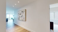 This well-appointed high-rise residence is thoughtfully designed across a single floor, offering a refined blend of modern finishes and functional living spaces. Light hardwood flooring flows throughout the main areas, complemented by crisp white walls and recessed lighting, creating a bright and cohesive aesthetic.

The open-plan kitchen and living room serves as the heart of the home. The kitchen is outfitted with sleek wood-grain cabinetry, a marble-style backsplash, stainless steel appliances including a gas range, and a generous island with seating — ideal for casual dining or entertaining. A wine refrigerator and city-facing window add further appeal.

The living area is expansive and airy, featuring floor-to-ceiling windows and access to an outdoor balcony, providing sweeping panoramic city views. Recessed lighting and clean architectural lines reinforce the contemporary feel throughout.

Both bedrooms are carpeted and bathed in natural light from large windows framing impressive urban skyline views. The primary bedroom offers a comfortable, serene retreat. A dedicated office space provides flexibility for work or study.

The two bathrooms are finished with marble-look tile, wood-toned cabinetry, and clean, neutral palettes. A hallway and closet complete the well-organized floor plan, ensuring practical storage and smooth circulation throughout.