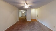Located at 110 Southport Rd in Spartanburg, SC, this single-floor residence offers a well-organized layout designed for comfortable living. The living room serves as a central gathering space, highlighted by a classic white-framed fireplace, plush carpeting, and a ceiling fan overhead. Vertical blinds cover a sliding glass door that opens to an outdoor area, allowing natural light to filter in. The open floor plan connects the living area to a dining space, both finished with neutral-toned carpet and ceiling fans throughout. The kitchen features wood-toned cabinetry, granite-style countertops, a breakfast bar peninsula, and black appliances including a refrigerator, stove, and microwave, with wood-look flooring completing the space. Bedrooms are carpeted and include ceiling fans and closet storage; one bedroom offers a built-in shelving closet system. A secondary bedroom provides natural light through a window with blinds. The primary bathroom is a standout, showcasing a corner soaking tub surrounded by mirrors, a granite-top vanity with an undermount sink, wood-look flooring, and a linen closet with wire shelving. Textured ceilings are consistent throughout the home, contributing to its traditional character.