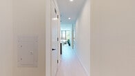 This single-floor residence showcases a refined contemporary design defined by clean lines, a crisp white palette, and an abundance of natural light. The open living area is anchored by dramatic floor-to-ceiling black-framed windows that frame lush outdoor tree views, flooding the space with daylight and creating a seamless connection to the surrounding environment. Light hardwood flooring runs throughout, contributing to a bright and airy atmosphere.

The galley-style kitchen is well-appointed with dark cabinetry, light quartz countertops, stainless steel appliances, and a deep undermount sink with a matte black faucet — a practical yet visually striking space for everyday use.

The bedrooms are generously proportioned and serene. The primary bedroom benefits from expansive windows overlooking mature trees, offering a tranquil retreat, and includes a double-door closet. A second bedroom provides ample storage and direct access to the main living area.

The bathroom presents a bold contrast of large-format light floor tiles against dark slate wall tiles, complete with a wall-mounted wood-toned vanity and a frameless mirror, delivering a spa-like aesthetic.

A clean, well-lit hallway connects each area of the residence, with recessed lighting and smooth white walls maintaining the space's cohesive, minimalist character throughout.
