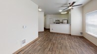 This single-floor unit offers a well-organized layout that balances open living spaces with defined private areas. The living room is generously proportioned, featuring rich wood-look flooring, a ceiling fan with light fixture, and multiple windows that allow abundant natural light to fill the space. A door provides additional access to the exterior, enhancing ventilation and connectivity.

The kitchen is positioned at the heart of the unit, separated from the living area by a peninsula that creates a natural open-concept flow. White shaker-style cabinetry with brushed nickel hardware lines the walls, complemented by light countertops and stainless steel appliances, including a refrigerator and electric range with overhead ventilation. A hallway extending from the kitchen leads to the remaining rooms.

The bedroom is carpeted for comfort, offering a mirrored sliding closet and a built-in desk ledge, with a window providing natural light. A dedicated bathroom is accessible from the bedroom area and features a full-size soaking tub with shower, a vanity with white cabinetry, light countertops, and a medicine cabinet mirror. Wood-look flooring extends throughout the bathroom, maintaining a cohesive aesthetic across the unit.