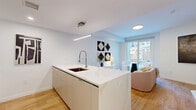 Located at 95 Anderson St in Hackensack, NJ, this thoughtfully designed single-floor studio presents a clean, modern aesthetic with an open-concept layout. The combined kitchen and living area forms the heart of the space, anchored by a sleek white kitchen island with a waterfall countertop, an undermount sink, and a professional-style pull-down faucet. A linear pendant light illuminates the island, which offers bar seating with contemporary dark-framed stools. The kitchen is fully equipped with stainless steel appliances, including a French door refrigerator, gas range, and built-in microwave, all set against crisp white cabinetry. Light hardwood flooring flows seamlessly throughout, enhancing the bright, airy ambiance created by white walls and recessed lighting. The living area benefits from a large window overlooking the surrounding streetscape, allowing natural light to fill the room. A cozy seating nook with a round bistro table and two accent chairs sits adjacent to the window. A dedicated sleeping area and a compact desk space provide functional versatility. The bathroom features large-format white tile flooring, white walls, and matte black fixtures, delivering a minimalist, spa-like feel. This well-appointed studio offers efficient, stylish urban living in a prime Hackensack location.