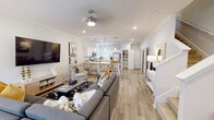 Located on Vista Dr in Clemson, SC, this two-story home offers a thoughtfully designed layout spread evenly across two floors. The main level features an open-concept living area with light wood-tone flooring, crown molding, and recessed lighting throughout. The spacious living room accommodates a large sectional seating arrangement and flows seamlessly into the kitchen, which is outfitted with white shaker cabinets, a subway tile backsplash, stainless steel appliances, and a breakfast bar with seating. A dedicated pantry with built-in shelving provides ample storage. A half bathroom and a stylish entryway with staircase access complete the first floor. Upstairs, the generous primary bedroom features plush carpeting, a ceiling fan, multiple windows for natural light, and closet access. The second bedroom is equally well-sized with its own closet. Both upper-level bathrooms are finished with white vanities, wood-look flooring, and lighted mirrors. Closets throughout are equipped with built-in wire shelving systems for organized storage. The home's neutral color palette, clean architectural lines, and consistent finishes create a bright, cohesive ambiance across all rooms.