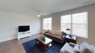 This well-designed single-floor residence in Frisco offers a thoughtful layout with modern finishes throughout. The living room serves as the heart of the home, featuring rich wood-look flooring, a ceiling fan with light, and multiple windows dressed with horizontal blinds that invite an abundance of natural light. The space comfortably accommodates a sofa, accent chair, and coffee table arrangement centered on a navy area rug, with a media console and flat-screen TV completing the setup.

The kitchen is a standout feature, showcasing a two-tone cabinetry design with dark espresso lower cabinets and lighter upper cabinets, accented by a mosaic tile backsplash. Stainless steel appliances, quartz countertops, and a generous island with seating provide both style and functionality.

The bedroom is a serene retreat, carpeted for comfort, with a ceiling fan, a large window, and a bold tufted leather headboard as a focal point. A dedicated office or flex space includes double doors and room for a desk and seating, offering versatility.

The bathroom is well-appointed with a full tub and shower surround featuring classic subway tile, wood-look flooring, a granite-topped vanity, and direct access to a spacious walk-in closet.