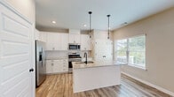 This two-bedroom, three-bathroom two-story home in Cartersville, Georgia offers a well-designed layout spread across two floors. The main level features an open-concept kitchen and living area with warm luxury vinyl plank flooring throughout. The kitchen is a standout, equipped with white shaker cabinetry, granite countertops, stainless steel appliances, a black matte sink faucet, a central island with pendant lighting, and a window that invites natural light into the space. Track lighting accents the living area, adding a modern touch. A half or full bathroom is also conveniently located on this floor, finished with matching LVP flooring and clean white fixtures. The attached garage offers a concrete floor and ample overhead lighting for practicality. Upstairs, the two bedrooms are carpeted and feature ceiling fans for comfort. The primary bedroom is generously sized and includes access to a dedicated closet with built-in wire shelving. Additional bedrooms connect to well-appointed bathrooms, including one with a tub-shower combination. Neutral tones throughout create a clean, move-in-ready aesthetic. The home's layout is efficient and functional, making it an ideal residence in the Cartersville community.