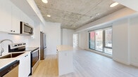 Located at 30 Rue Jos-Montferrand in Gatineau, this modern 2-bedroom, 2-bathroom unit offers a thoughtfully designed open-concept layout with a clean, contemporary aesthetic. The living and kitchen area is anchored by a striking exposed concrete ceiling with recessed lighting, which contrasts beautifully against crisp white walls and light wood-style flooring that flows throughout the space. The kitchen is well-appointed with white cabinetry, stainless steel appliances including a refrigerator, electric range, built-in microwave, and dishwasher, alongside a central island with a light countertop that doubles as a breakfast bar. Large floor-to-ceiling windows in the living area and bedrooms flood the space with natural light and frame urban views of the surrounding Gatineau cityscape. The primary bedroom features an exposed concrete ceiling accent, a built-in closet, and direct access to natural light. The second bedroom also benefits from generous windows with city views and ample closet space. The two bathrooms are finished in neutral tones: one features a sleek glass-enclosed walk-in shower with large-format tiles, while the other offers a full soaker tub with tiled surround. A hallway connects the rooms efficiently, completing this well-organized and stylish urban residence.