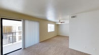 This two-story space is designed with practicality and comfort in mind. The main living area features wall-to-wall carpeting in a neutral beige tone, providing a warm and inviting foundation throughout. Light yellow walls contribute to a bright, airy atmosphere, complemented by a textured white ceiling that adds subtle visual interest overhead.

A ceiling fan is centrally positioned in the living area, offering both air circulation and a modest decorative element. Natural light enters the space through a window fitted with horizontal blinds, allowing for adjustable brightness and privacy. A set of vertical blinds lines one wall, concealing what appears to be a sliding glass door that likely provides access to an outdoor area, enhancing the connection between interior and exterior.

HVAC vents are visibly integrated into the walls, indicating a central climate control system throughout the space. The overall layout appears open and unobstructed, providing flexible options for furniture arrangement. The two-floor configuration suggests additional living or sleeping areas on the upper level. The neutral color palette and clean finishes give the space a move-in ready quality suitable for a variety of lifestyles.
