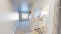 Located in the Lake City neighborhood of Seattle, WA, this one-bedroom, one-bathroom residence offers a smart and efficient layout designed to maximize every square foot. The open entry transitions seamlessly between the kitchen and the carpeted living area, which benefits from a large window that draws in natural light and provides views of the surrounding greenery.

The kitchen is thoughtfully designed with white cabinetry, light stone-toned countertops, and a full suite of white appliances including a refrigerator, electric range, over-the-range microwave, and dishwasher. Light wood-style flooring grounds the kitchen space, offering a clean contrast to the soft carpet in the living area.

The bedroom is a comfortable, well-proportioned retreat featuring plush carpet, a large window with blinds for privacy, and a sliding-door closet with built-in shelving. The room connects conveniently to the rest of the unit, maintaining a practical flow throughout.

The bathroom is finished with neutral warm tones, light wood-style flooring, a granite-style vanity countertop, and chrome fixtures, giving it a clean and polished feel. Overall, the unit presents a bright, neutral palette with a cohesive and functional design well-suited for comfortable everyday living.