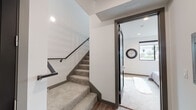This two-story residence in Los Angeles offers a thoughtfully designed layout with modern finishes throughout. The open-concept main level features warm hardwood-style flooring that flows seamlessly from the living and dining areas into the kitchen. The living room is anchored by large sliding glass doors that open to a private balcony, allowing abundant natural light and views of the surrounding palm tree-lined neighborhood. The kitchen is outfitted with two-tone cabinetry — high-gloss white upper cabinets paired with dark wood lower cabinets — complemented by a metallic tile backsplash, clean white countertops, and a full suite of stainless steel appliances including a gas range, dishwasher, microwave, and refrigerator. Carpeted stairs lead to the upper level, where the bedrooms offer a quiet retreat. Each bedroom features plush carpeting and recessed lighting, with windows framing views of nearby palm trees. The bathroom is finished with elegant marble-style tile lining the tub surround and walls, paired with a frameless glass enclosure for a clean, upscale aesthetic. Throughout, the design maintains a cohesive contemporary style with clean lines, neutral tones, and quality finishes that reflect the character of modern Los Angeles living.