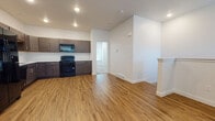 This well-appointed two-floor residence offers a clean, modern aesthetic with thoughtful design details throughout. The main living area features warm wood-look luxury vinyl flooring that flows seamlessly from the open-concept living space into the kitchen. The kitchen is equipped with dark espresso-toned cabinetry, white countertops, and a full suite of black appliances including a refrigerator with ice maker, electric range with over-the-range microwave, dishwasher, and a single-basin sink — providing everything needed for everyday cooking and entertaining.

The open layout between the kitchen and living area creates a spacious, connected feel, with recessed lighting overhead adding a bright, contemporary touch. A staircase with a neatly finished half-wall railing connects the two floors, maintaining an airy, open sightline.

The upper floor hosts a generously sized bedroom with plush neutral carpet, recessed lighting, and a window dressed with blinds that allows natural light to fill the room. Two bathrooms serve the unit — one featuring a vanity with a marble-style countertop and wood-look flooring, and another with a full soaking tub and shower combination in crisp white. Throughout, the interiors are finished in clean white walls and white trim, lending the space a fresh, move-in-ready quality.