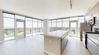 Located at Harbor Point in Stamford, CT, this thoughtfully designed 2-bedroom, 2-bathroom residence offers a refined living experience with modern finishes and breathtaking water views. Light wood-tone flooring runs throughout the space, creating a warm and cohesive aesthetic.

The open-concept kitchen and living area serves as the heart of the home. The kitchen is outfitted with stainless steel appliances, warm wood cabinetry with textured detail, white quartz countertops, a subway tile backsplash, and a central island ideal for dining or entertaining. Track lighting adds a contemporary accent overhead.

The living area is bathed in natural light, thanks to expansive floor-to-ceiling windows that frame sweeping panoramic views of the waterfront and surrounding greenery—a defining feature of this residence.

The generously sized primary bedroom offers direct access to a well-appointed en-suite bathroom, complete with a sleek double vanity featuring an illuminated mirror, grey cabinetry, light wood-tone flooring, and a frameless glass-enclosed shower. A dedicated closet provides ample storage.

The second bedroom is bright and versatile, featuring a sliding closet and neutral walls. The second bathroom is efficiently designed with a vanity, illuminated mirror, and shower-tub combination. Throughout, the clean, neutral palette creates a calm and inviting atmosphere.
