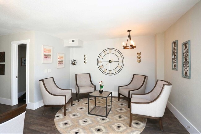 Community seating area with upholstered chairs, round rug, coffee table, wall decor, and modern chandelier lighting - Bennett Pointe