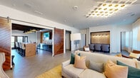 Located at 150 Mill Creek Pkwy in LaGrange, Georgia, this thoughtfully designed single-floor amenity space offers a sophisticated blend of comfort and functionality across several distinct areas. The spacious living room serves as the heart of the space, anchored by a striking geometric lattice ceiling fixture with gold accents that draws the eye upward. Large windows dressed in sheer curtains flood the room with natural light, complementing the neutral-toned sectional seating, woven area rugs, and a built-in shelving unit housing a flat-screen TV and coffee station. Clustered mirrors and curated décor add an artistic touch throughout. Two separate dining areas provide flexible gathering options. One features bold navy-blue wainscoted walls, a light wood dining table with leather chairs, a wood-planked ceiling, and oversized pendant lights — creating an intimate yet refined atmosphere. A kitchenette area is highlighted by a one-of-a-kind backsplash crafted from cross-sectioned wood rounds, paired with grey cabinetry and a mounted TV. An additional room offers a game area, defined by dramatic sliding barn doors with a herringbone wood pattern and exposed dark wood beam ceiling details, adding a rustic-industrial contrast to the overall modern aesthetic. Large-format tile flooring runs throughout, unifying the entire space.