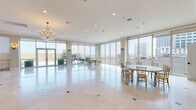 Located in the heart of New Orleans, this Grand Ballroom and Rooftop Pool Deck offers a sophisticated event venue with breathtaking panoramic views of the city skyline. The main ballroom is a bright, open space defined by floor-to-ceiling glass windows and walls on multiple sides, flooding the interior with abundant natural light while showcasing sweeping views of the surrounding cityscape. Polished marble tile flooring with decorative inlay accents runs throughout, reflecting light and enhancing the sense of grandeur. Elegant crystal chandeliers hang from the smooth white ceiling, complemented by recessed lighting and gold-toned wall sconces that create a warm, refined ambiance. Gold Chiavari chairs and round banquet tables are arranged throughout, making the space well-suited for receptions, galas, and corporate events. A large flat-screen display is mounted in a secondary gathering area, which also features a tray ceiling with crown molding for added architectural detail. The fully equipped catering kitchen is outfitted with rich cherry wood cabinetry, granite countertops, stainless steel appliances including a full range, refrigerator, and dishwasher — ideal for supporting large-scale events. Glass doors open directly onto the rooftop pool deck, seamlessly connecting indoor elegance with outdoor entertaining possibilities above the New Orleans skyline.