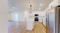 Located at 6155 24th St S in Fargo, ND, this well-appointed 4-bedroom, 2-bathroom single-floor residence offers a clean, modern aesthetic throughout. The heart of the home is a beautifully designed kitchen featuring crisp white shaker cabinetry, light quartz countertops, a center island, and a full suite of stainless steel appliances including a range, microwave, dishwasher, and refrigerator. A stylish multi-bulb pendant chandelier adds a refined touch overhead, while light-toned hardwood-style flooring flows seamlessly through the main living areas. The open living room is bright and welcoming, illuminated by recessed lighting and a sliding glass door that leads to a private balcony with outdoor views. The four bedrooms are carpeted for comfort, with large windows that fill each room with natural light and offer pleasant exterior views. The primary bedroom includes a walk-in closet with wire shelving. Both bathrooms are finished with warm wood-look flooring, white cabinetry with dark hardware, and tub-shower combinations. The consistent use of white walls, neutral tones, and modern fixtures creates a cohesive, contemporary feel throughout the entire home.