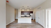 This thoughtfully designed single-floor residence offers a cohesive blend of modern finishes and functional layout. The open-concept kitchen serves as the heart of the home, showcasing rich dark-espresso cabinetry extending to the ceiling for generous storage, light quartz countertops, and a full suite of stainless steel appliances including an electric range, built-in microwave, and a French door refrigerator with ice and water dispenser. A large central island with a sink and pendant lighting above provides additional prep space and casual seating, flowing seamlessly into the living and dining areas, all finished with durable wood-look plank flooring. The living area is open and airy, with neutral warm-toned walls and room for a variety of furniture arrangements. The bedrooms are carpeted for comfort, each featuring large windows that invite abundant natural light and ceiling fans for climate control. The primary bathroom is spacious and functional, with dark cabinetry, a dual-sink vanity with quartz countertops, wood-look flooring, and direct access to a walk-in closet with built-in shelving. Throughout, the neutral color palette, clean lines, and consistent finishes create a cohesive and move-in-ready living environment.